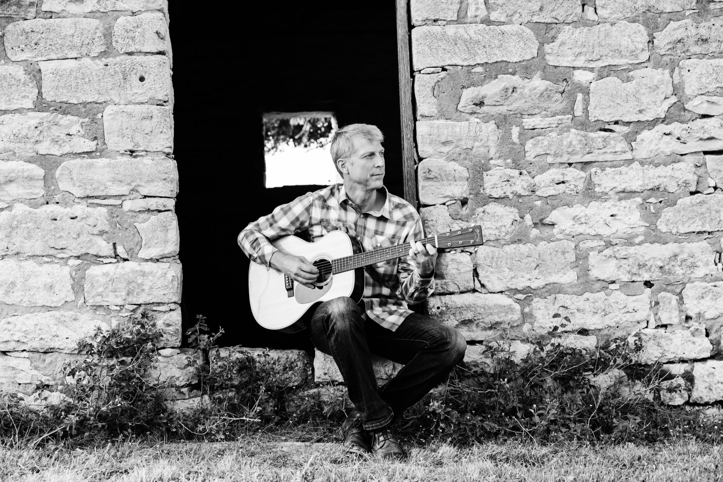 Ian playing guitar in a doorway, in black and white
