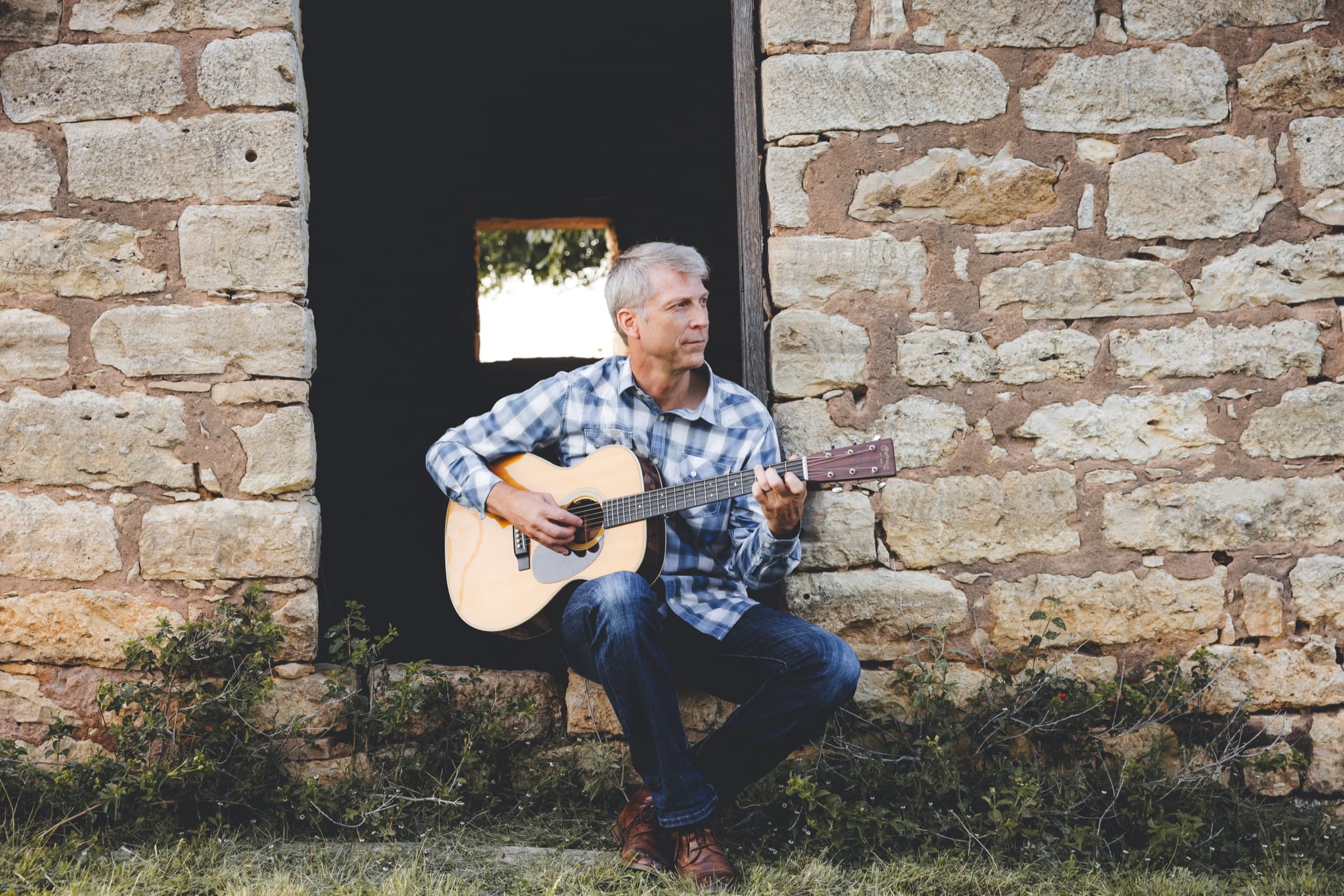 Ian playing guitar while sitting in a stone doorway