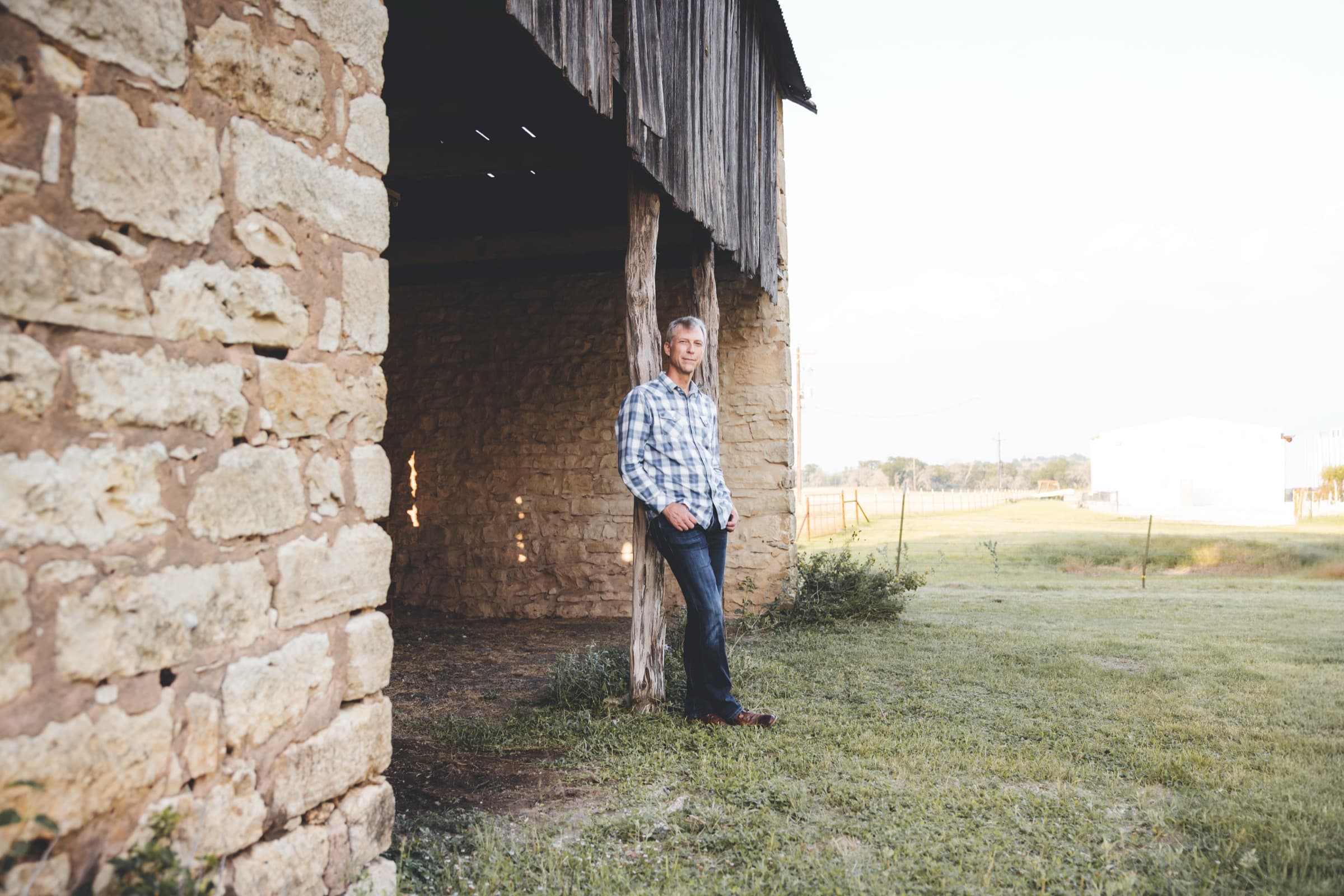 Ian leaning on a cedar post beside a stone barn