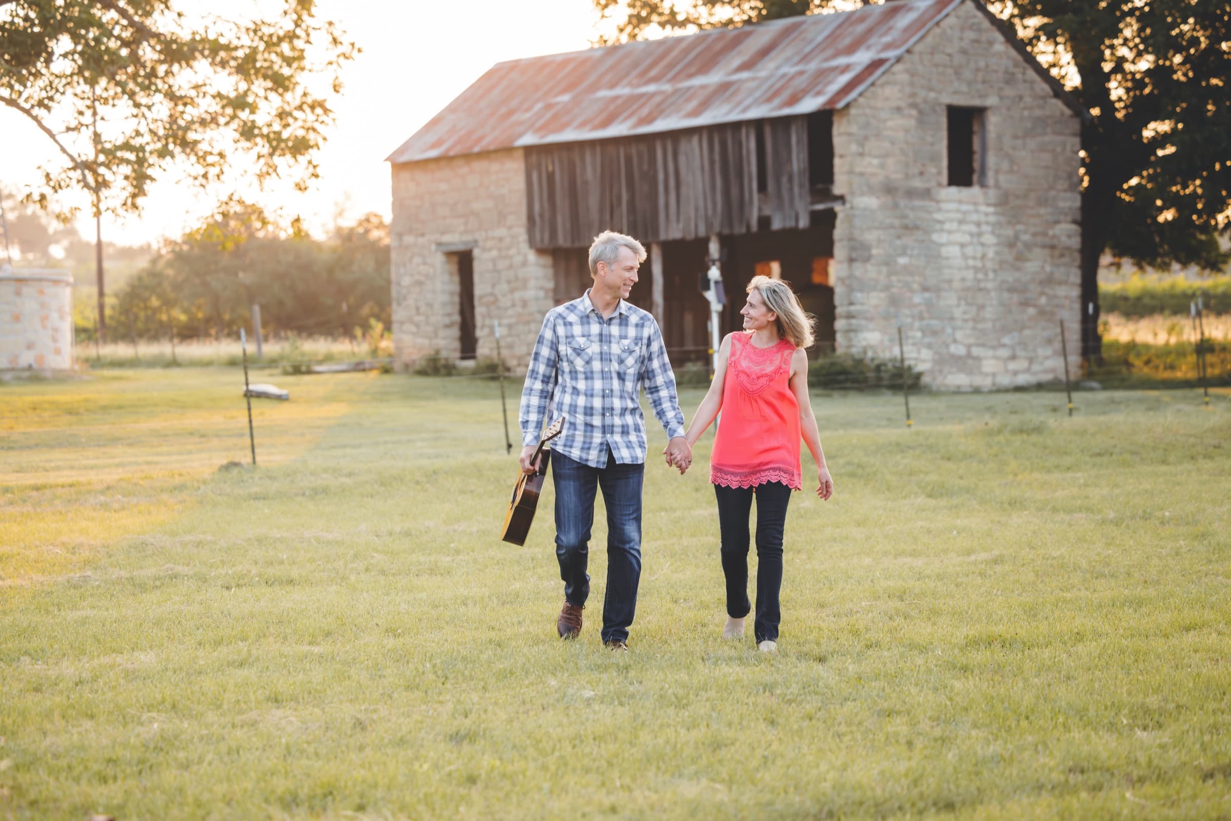 Ian walking hand in hand through a field at sunset, guitar at his side